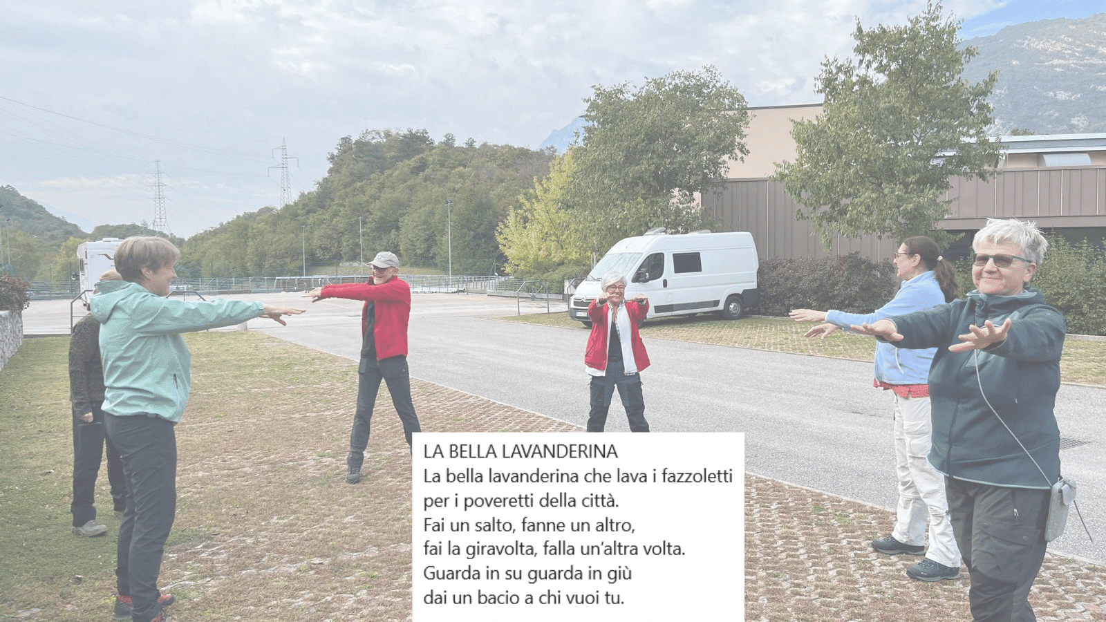 6 Personen stehen auf einem Parkplatz, im Hintergrund zwei Camper und ein Gebäude. Sie machen Gymnastik. Im Vordergrund die ersten Zeilen eines italienischen Kinderlieds.